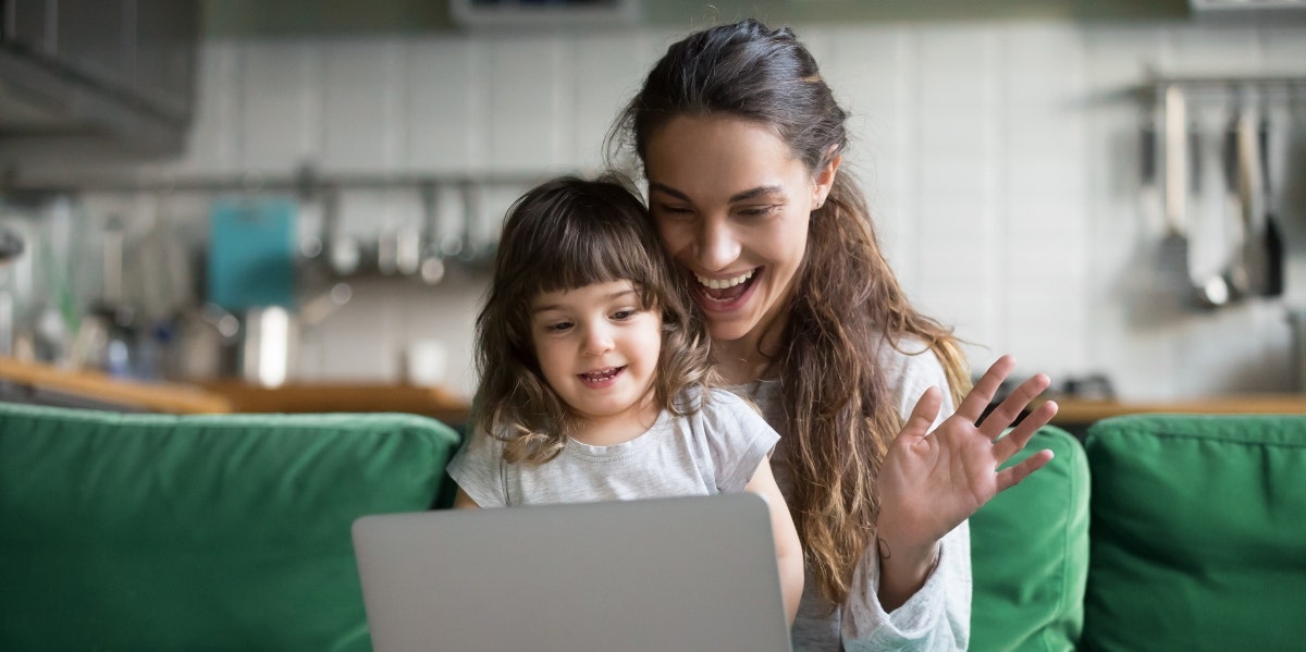 work from home moms mom waving at computer with daughter on her lap