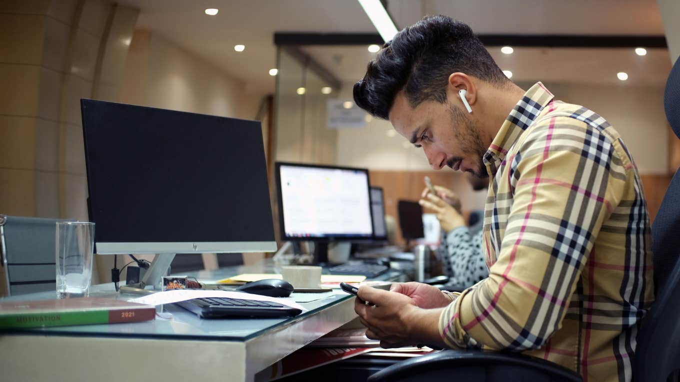 man at computer looking at his phone 