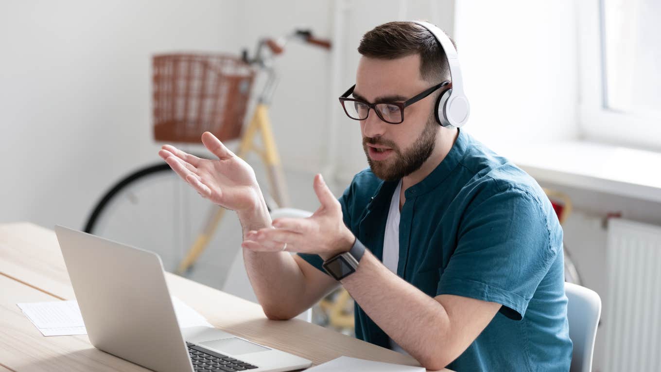 Focused young businessman in eyewear wearing headphones, holding video call with clients on lapto