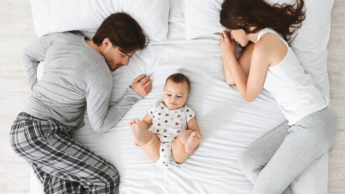 Working Dad Asks Stay-At-Home Wife For Weekend Mornings Off From Taking Care Of Their Newborn couple sleeping in bed with baby between them