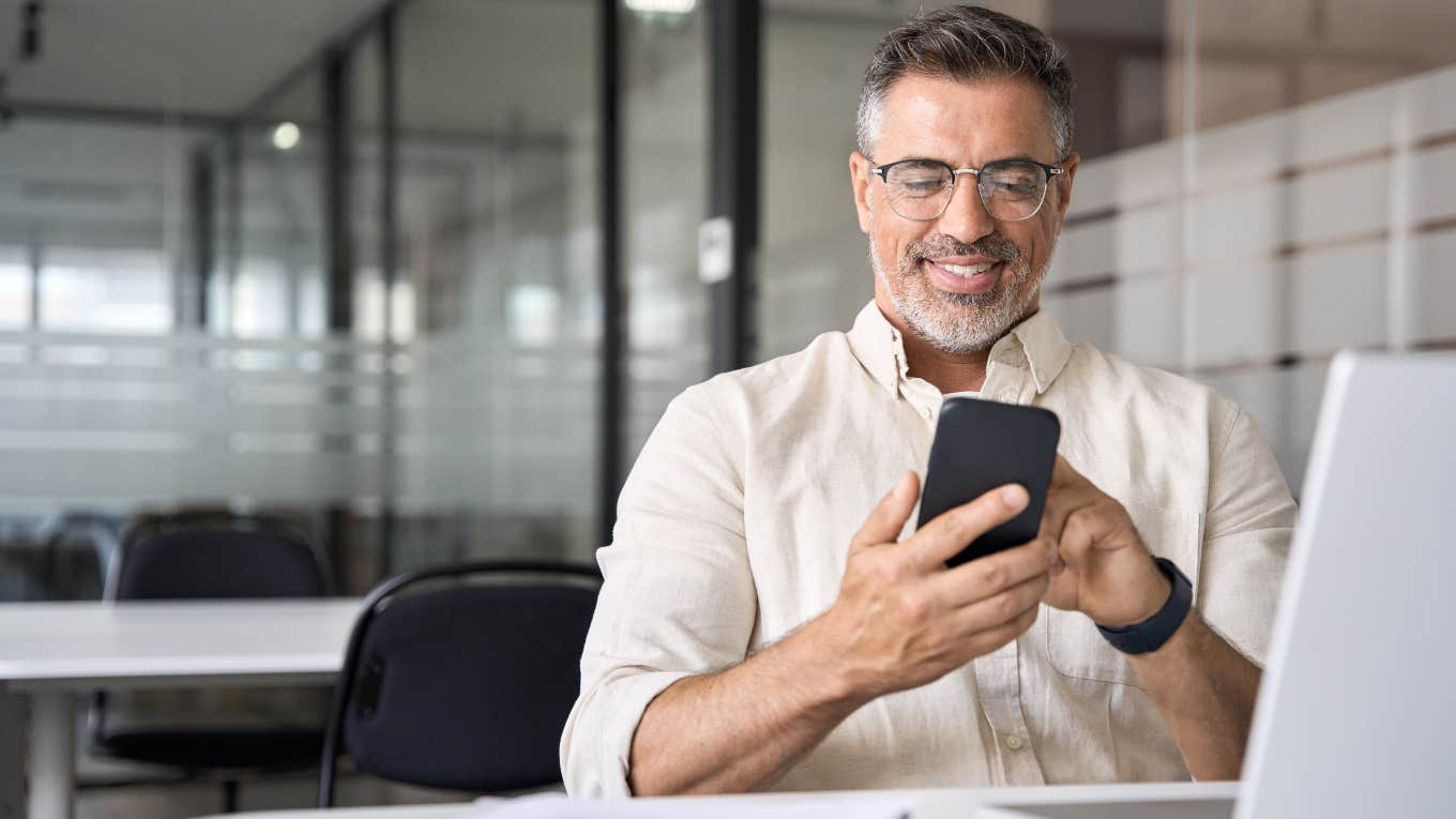 older man using cell phone while on his computer