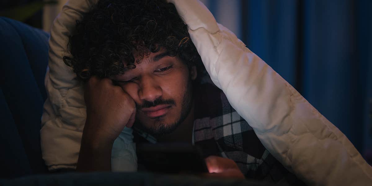I Found Out My Amazing Ex Was Pregnant ... On Facebook unhappy guy looking at phone under covers