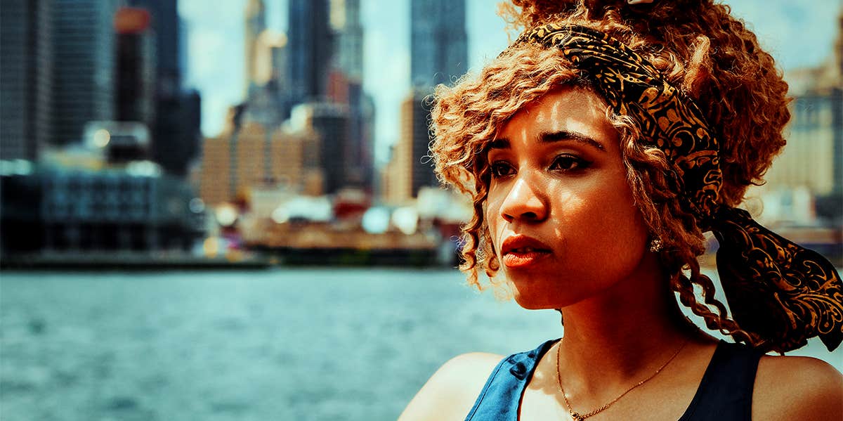 Your Trauma Is Your Training woman standing outside by water in city