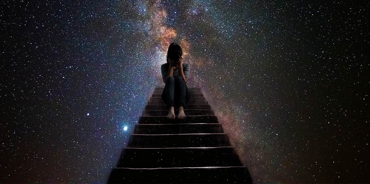 sad woman sitting on stairs with galaxy behind her