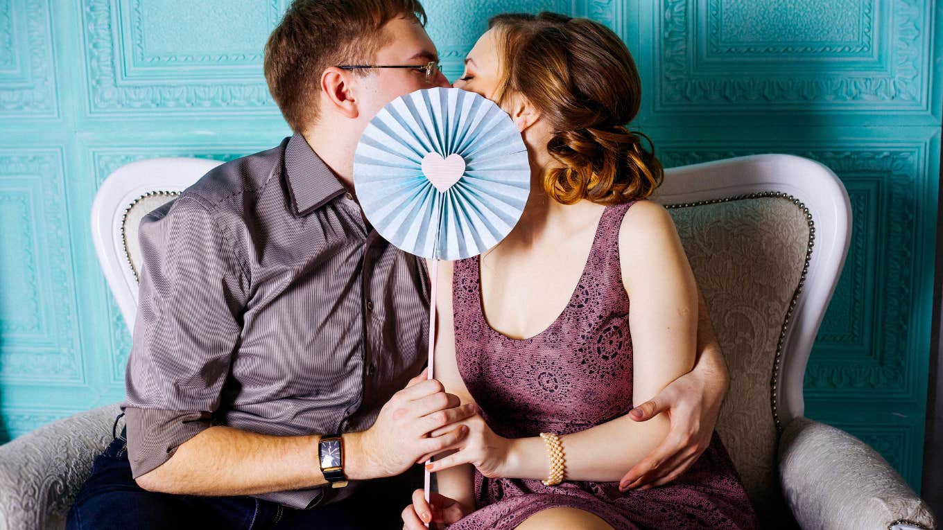 couple kissing behind fan with blue heart