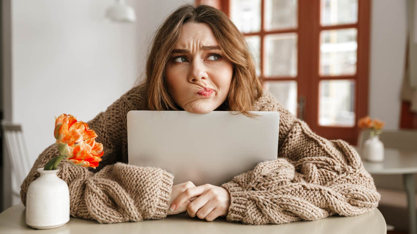 woman in sweater with computer looking uncertain