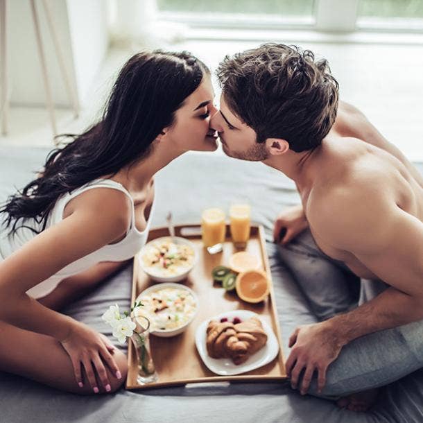 couple kissing while eating breakfast in bed