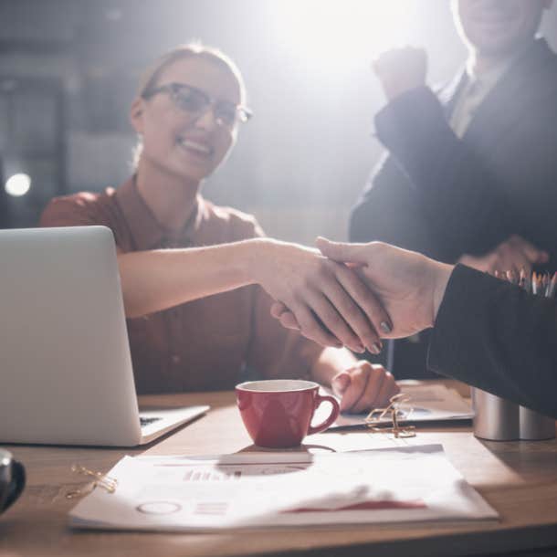 Woman shaking a man's hand in a professional setting featuring a coffee mug.