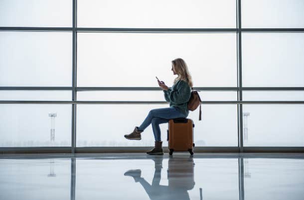 woman sitting on luggage using her phone at the airport