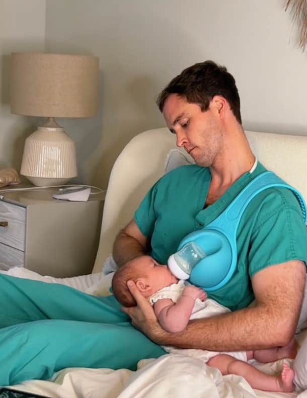 man feeds baby on the bed in his scrubs