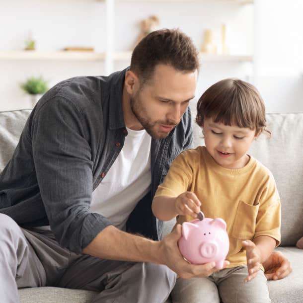 A father holds out a piggy bank for his son who slips a coin inside.