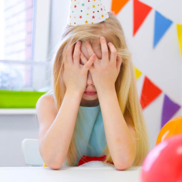 Unhappy blonde caucasian girl is crying face near birthday rainbow cake. Festive colorful background. Bad birthday party.