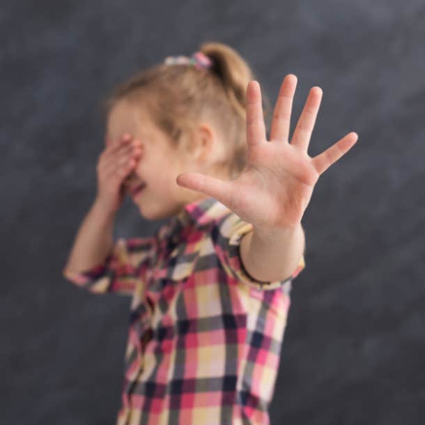 Little girl covering her eyes and gesturing "stop" with her hand. 