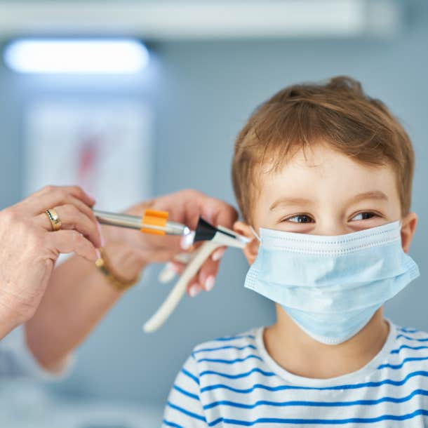 A doctor is checking the ear canal of a child wearing a disposable mask.