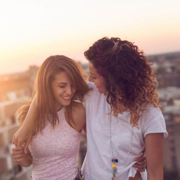 Couple standing and hugging on a building rooftop at sunset with a cityscape in the background.