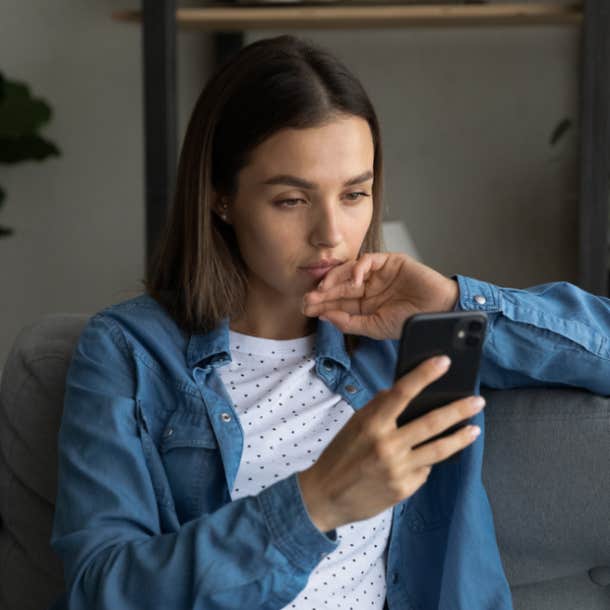 A young woman sits on a sofa and looks into her phone pensively.