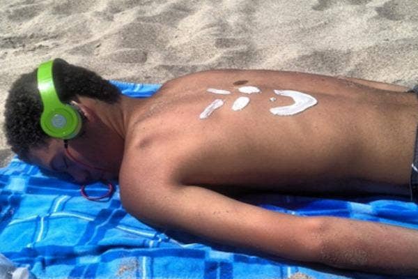 Man asleep on beach, with word spelled out on his back with sunblock.