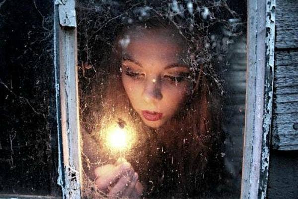 woman peeks through cobwebbed window