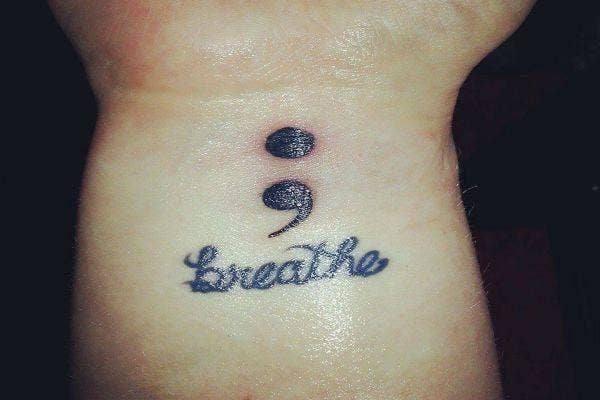 Arm tattoo of semicolon and the word breathe.