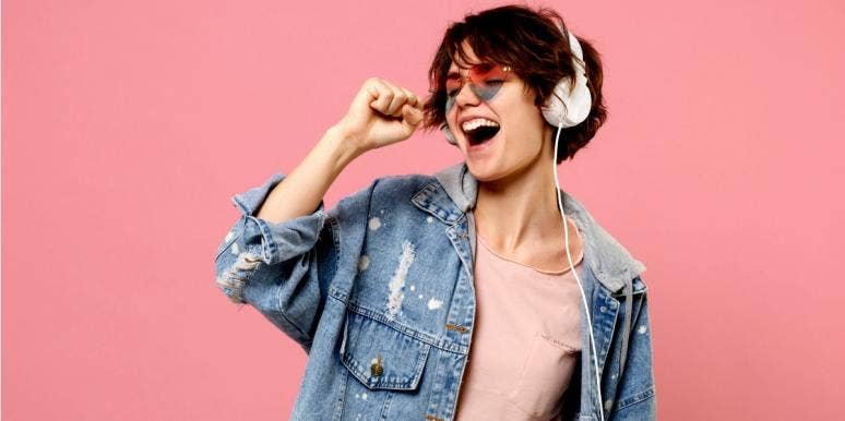 100 Best Love Songs From The 2000s & 2010s To Play On Repeat woman listening to music on headphones with pink background