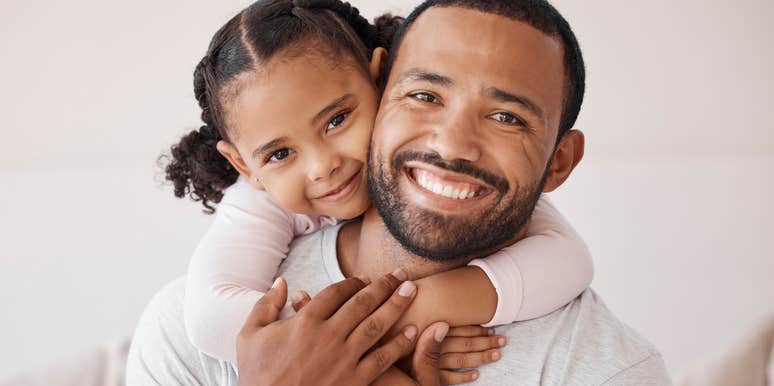 smiling dad holding young daughter raising her to be confident
