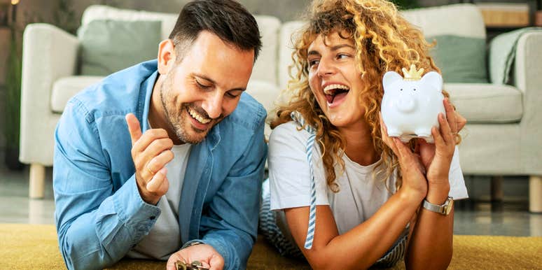 Happy couple smiling and playing with money, with woman holding a piggy bank, showing how to make money conversations in marriage easier.