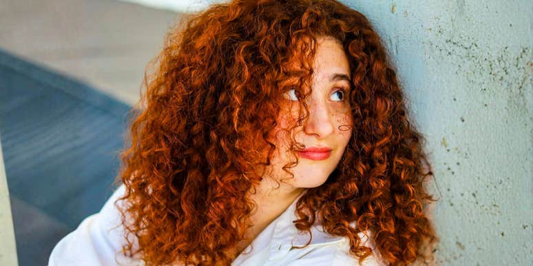 Confident, composed woman with red curly hair outdoors showing the art of emotional command and habits of people who stay present in tough times.