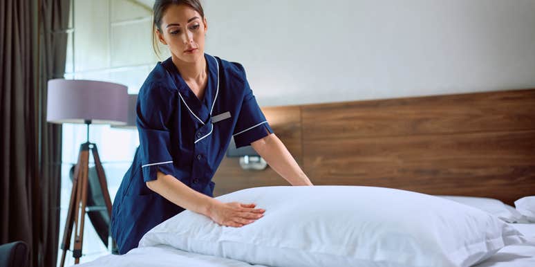 young female housekeeper at hotel making bed