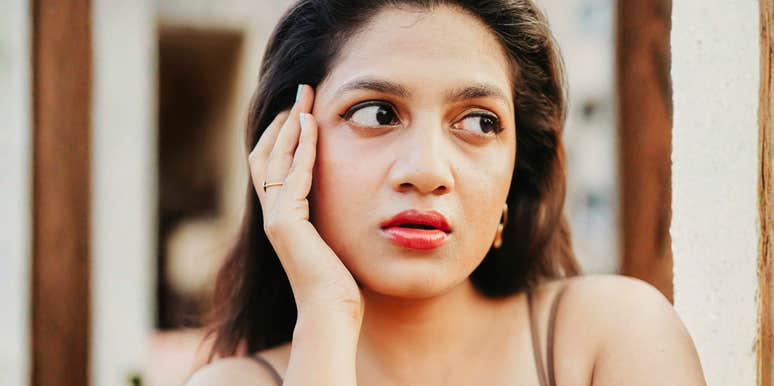 Woman resting her face in her hands while looking off to the side with a thoughtful, uncertain expression.