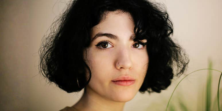 Woman with short dark hair standing indoors in soft natural light, looking ahead calmly.