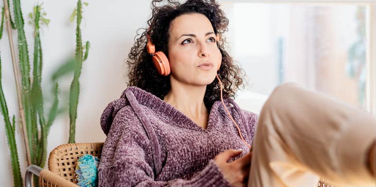 Woman sitting indoors listening to music and thinking, representing people who wonder whether certain thoughts or habits could be OCD, as an OCD specialist explains what OCD actually is.