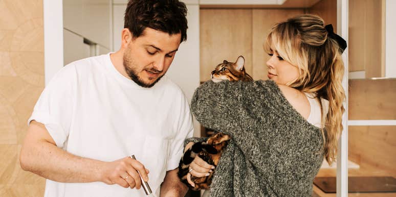 Couple navigating a playful, chaotic kitchen moment with a cat showing the real-life cat-and-dog messiness behind how partners fight fair.