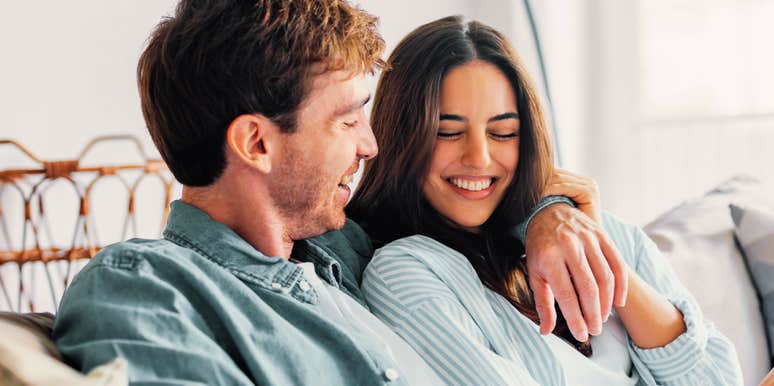 Couple sitting close together on a couch, smiling and relaxed during a quiet moment at home.