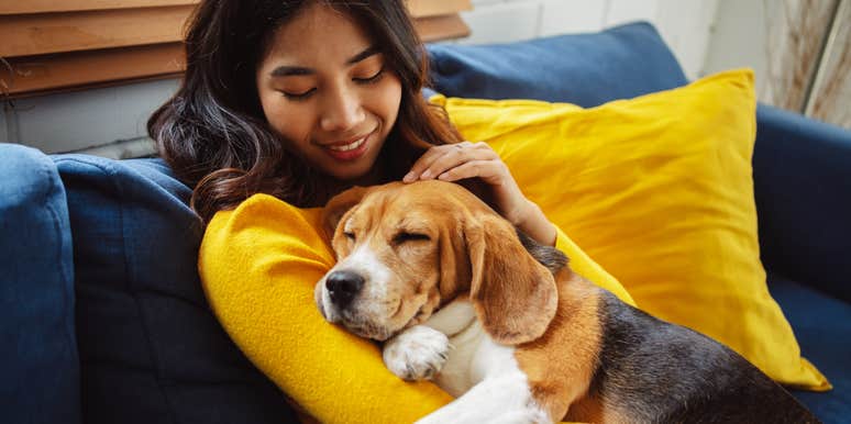 woman cuddling with sleeping dog on couch at home