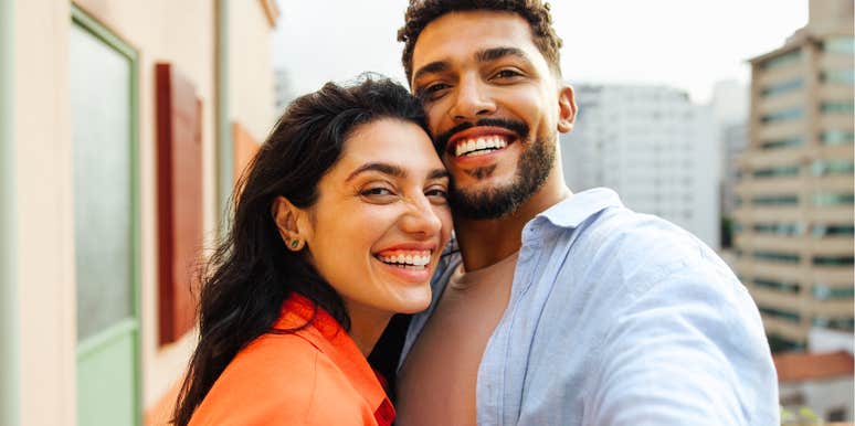 Smiling couple taking a selfie together outdoors in a city setting.