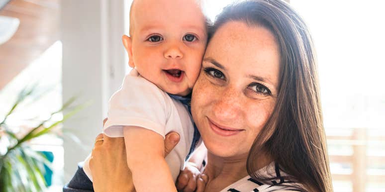 Woman holding a baby indoors near a window.