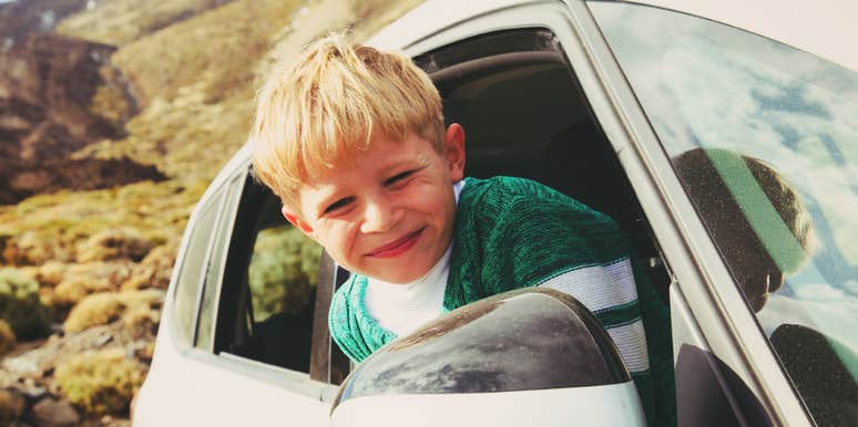 Smiling child leaning out of a car window during a road trip