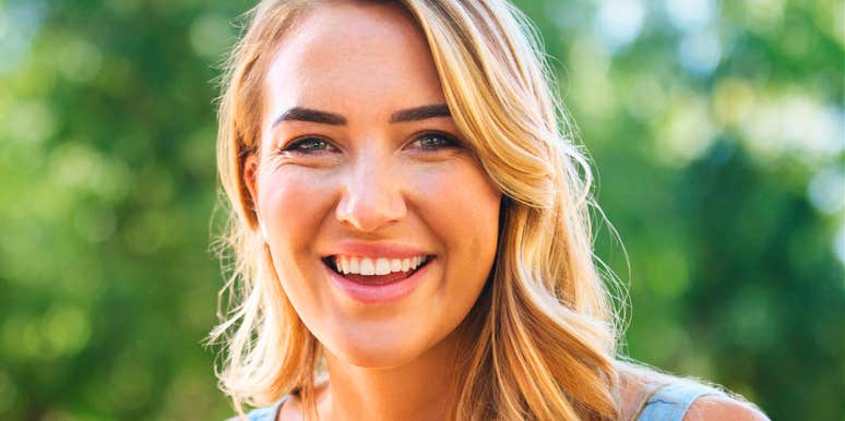 A smiling woman outdoors with greenery in the background.