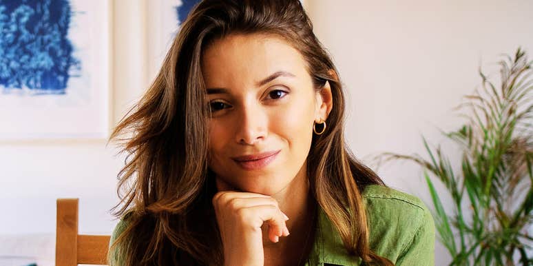 A woman sitting at a table inside a home, resting her chin on her hand.