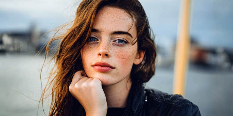 A woman with a calm, reflective expression standing outdoors, appearing thoughtful and emotionally grounded.