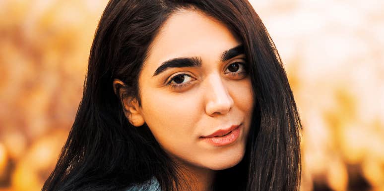 A woman with dark hair looking toward the camera outdoors in warm light.
