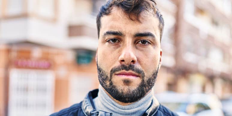 Man looking directly at the camera outdoors on a city street.