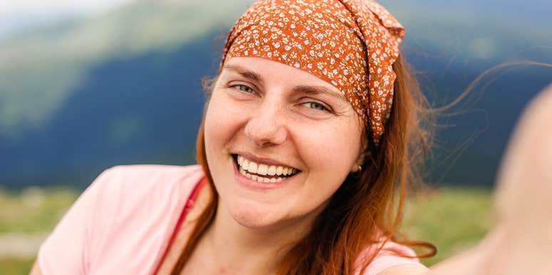 A woman smiling outdoors with mountains in the background.