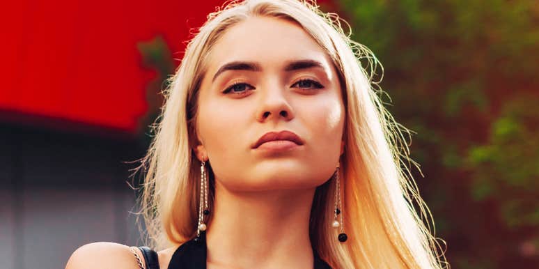 Serious-looking woman with blonde hair gazing confidently at the camera outdoors, conveying intensity and control