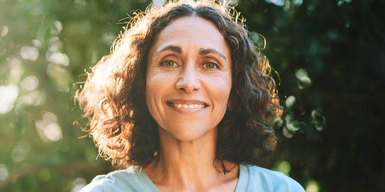 A calm, confident woman over fifty smiling gently outdoors, reflecting self-assurance, presence, and the kind of quiet confidence that earns lasting respect.