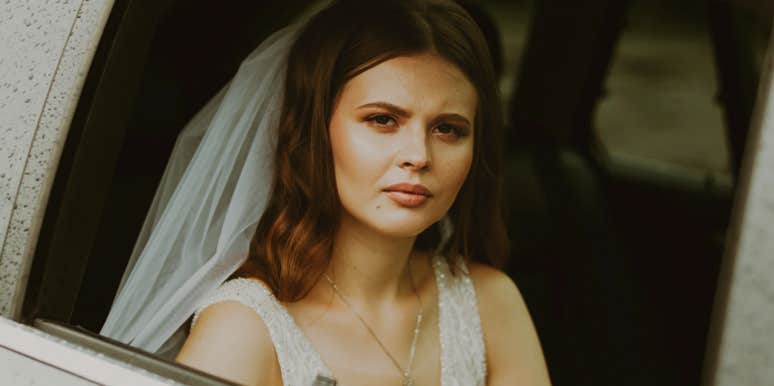 A bride in a wedding dress looking out of a car window.