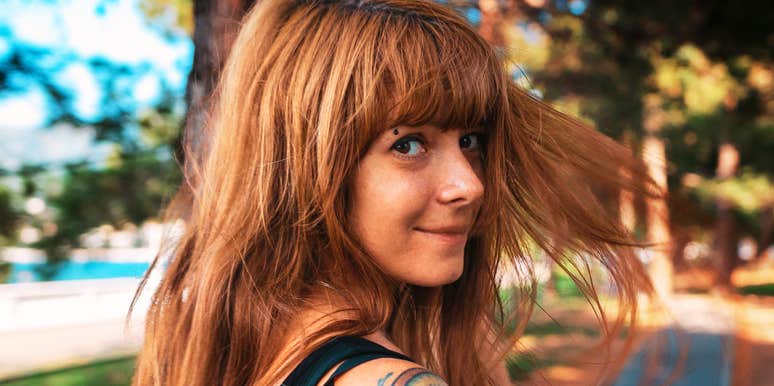 Woman glancing over her shoulder outdoors with a subtle, knowing expression.