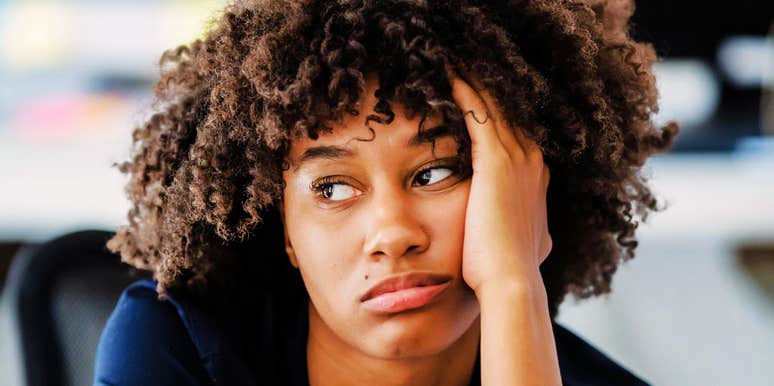 A woman with curly hair resting her head on her hand and looking off to the side.