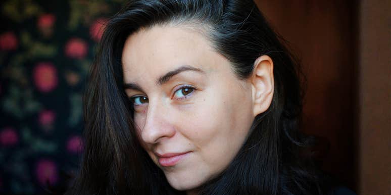 Close-up portrait of a woman with dark hair and a calm expression, photographed in soft natural light.