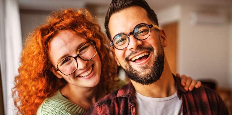 A smiling couple standing close together indoors.